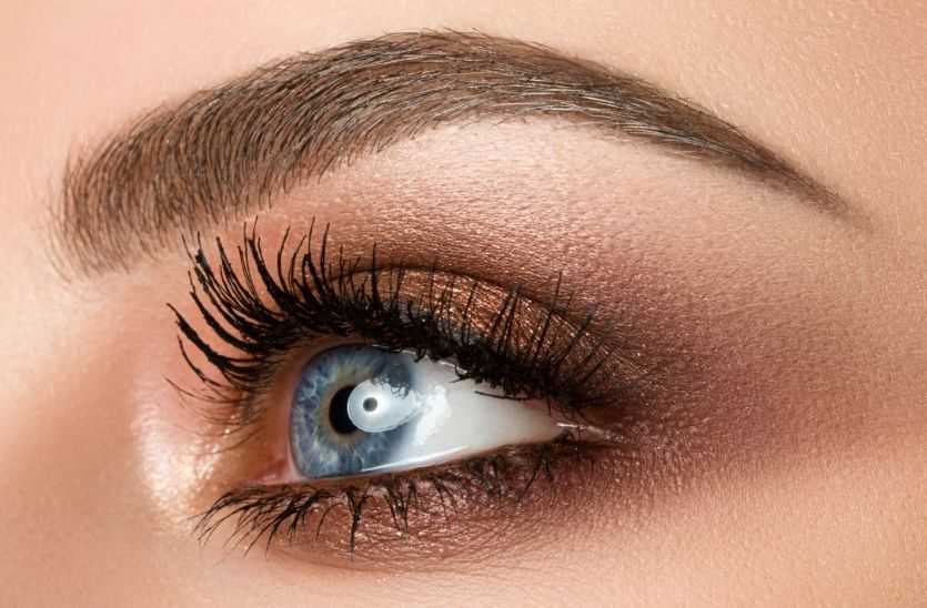 Close-up of a blue eye with detailed makeup, highlighting brown eyeshadow and long lashes.