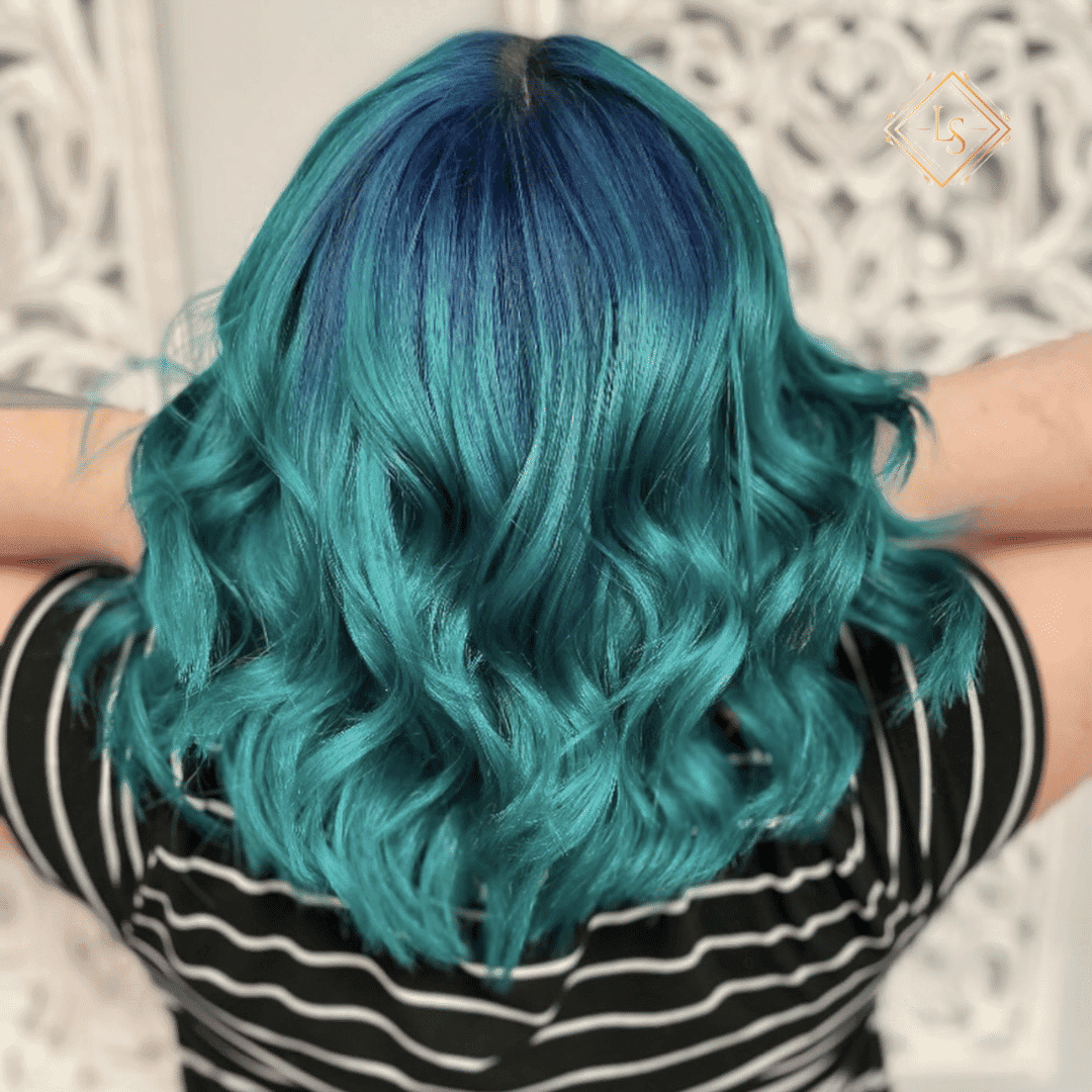 Woman with vibrant blue and teal wavy hair, wearing a black and white striped shirt.