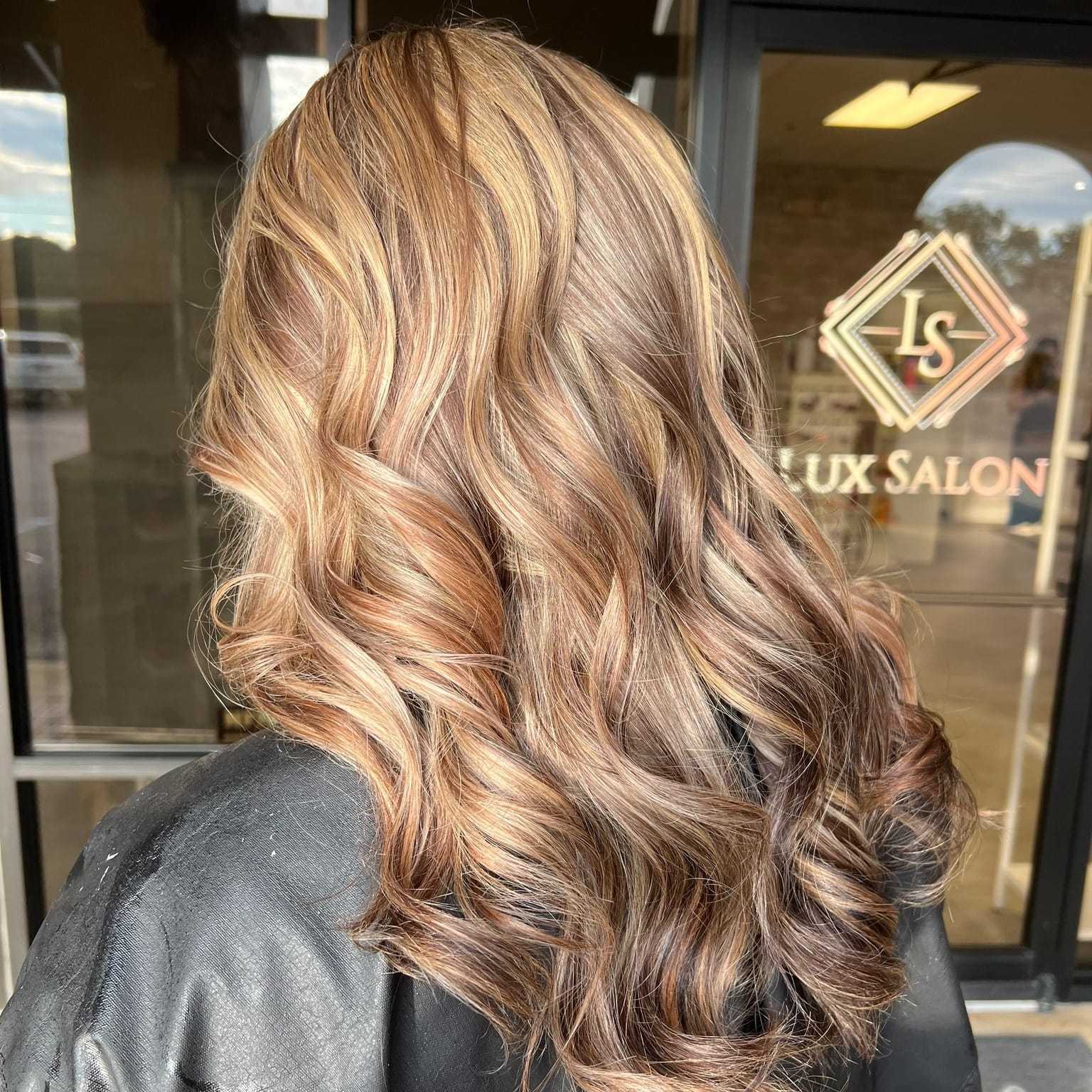 Woman with wavy blonde highlights in her brown hair at Lux Salon.