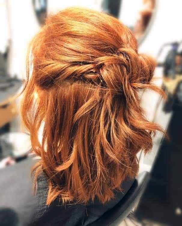 Woman with auburn hair styled in a half-up braided bun, seated in a salon chair.